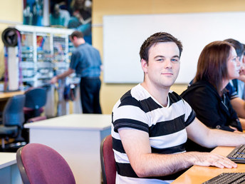 A photograph of a student in a classroom sitting in front of a computer